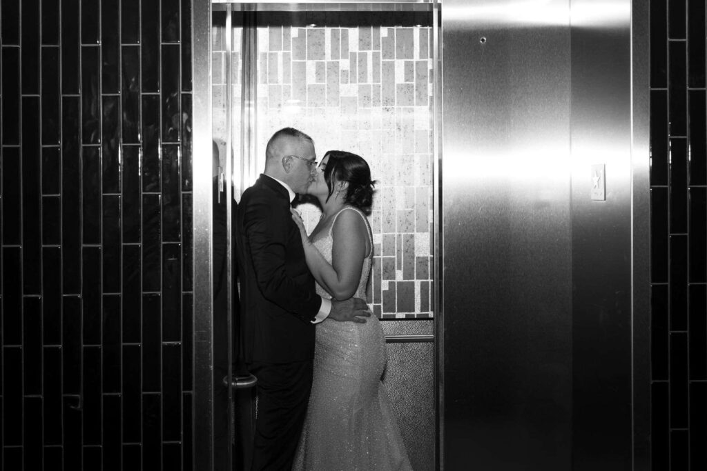 Mariés s'embrassant dans un ascenseur, photo de mariage noir et blanc style paparazzi.